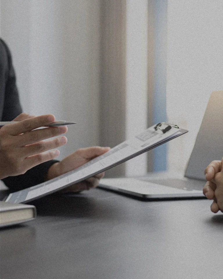 Twee mensen in gesprek terwijl ze een notitieblok en laptop gebruiken aan tafel.